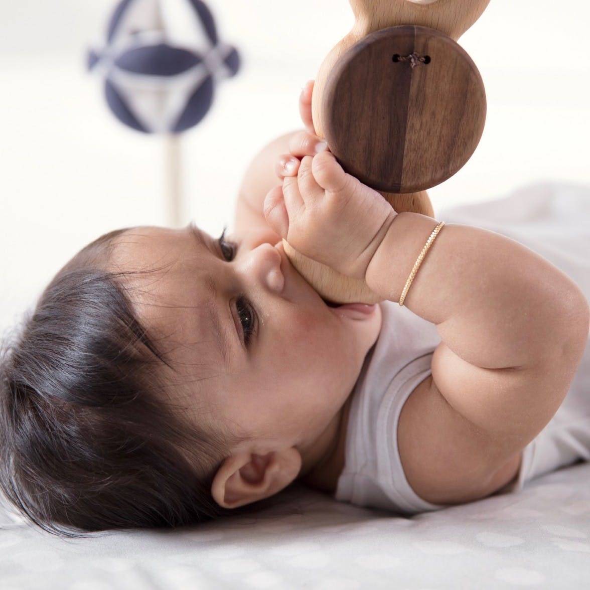 A baby laying on its back chewing on the Batting Ring from the Play Gym by Lovevery