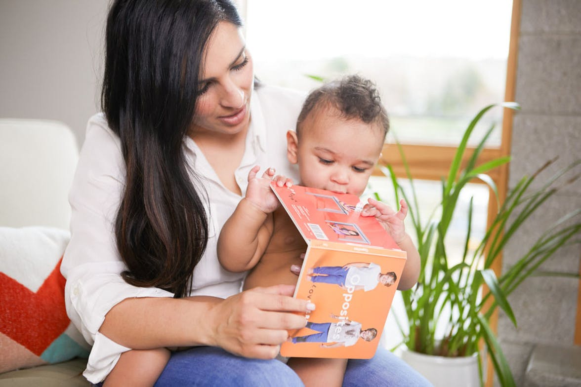 Woman holding a baby in their lap while looking at a book about opposites by Lovevery.