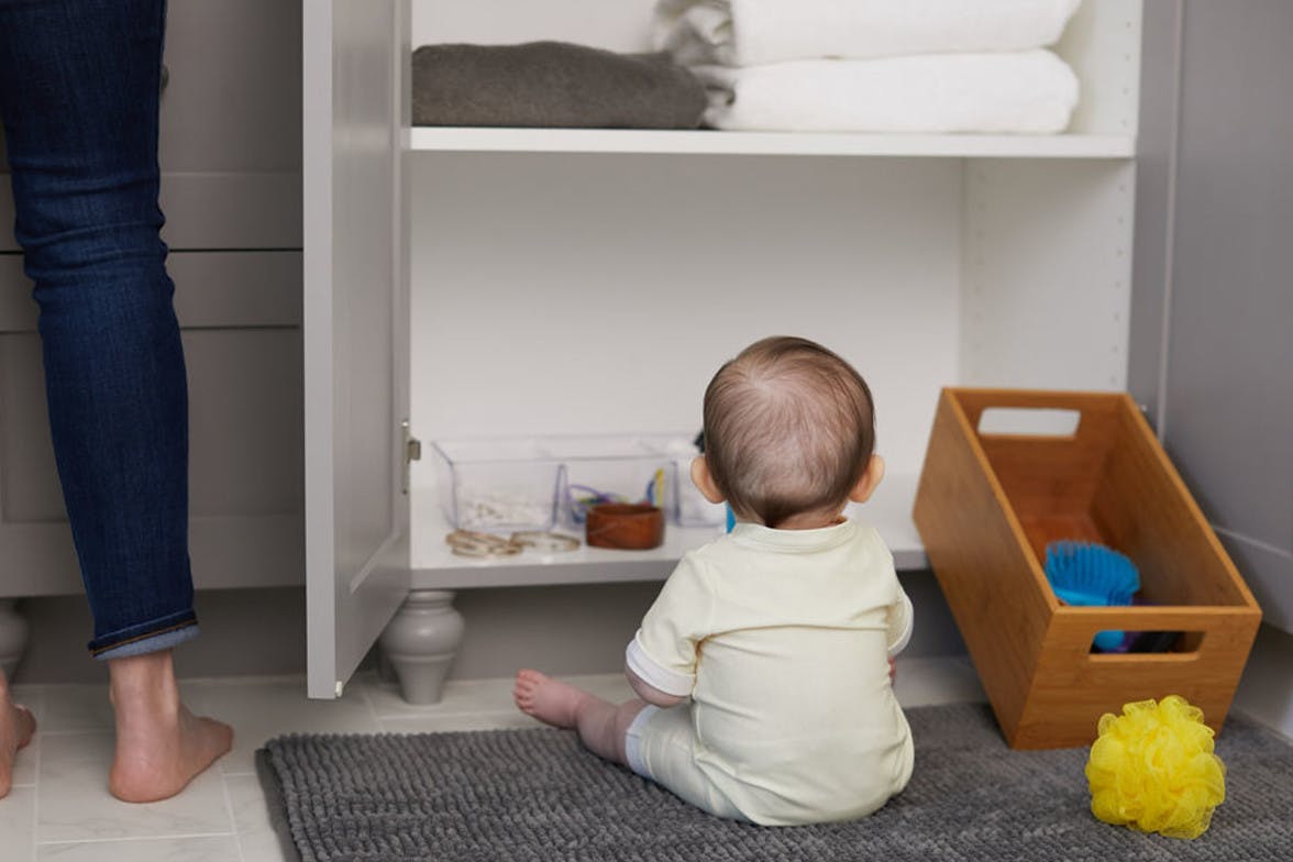 Baby sitting up and looking into an open bathroom cabinet