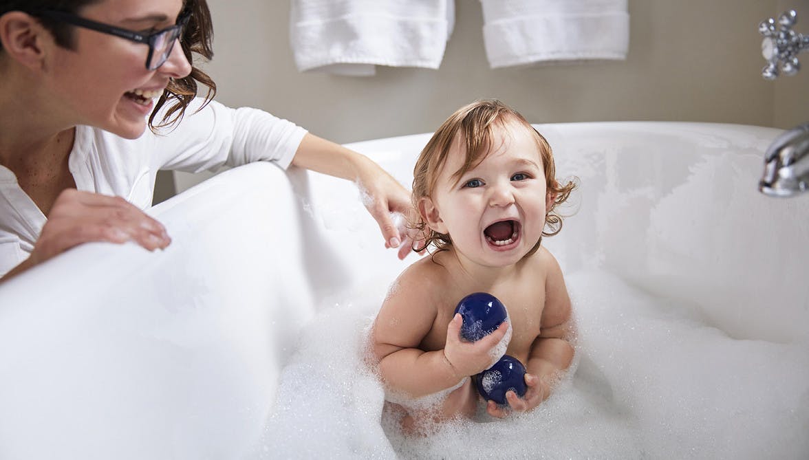Toddler in a tub playing with the Opposite Balls by Lovevery