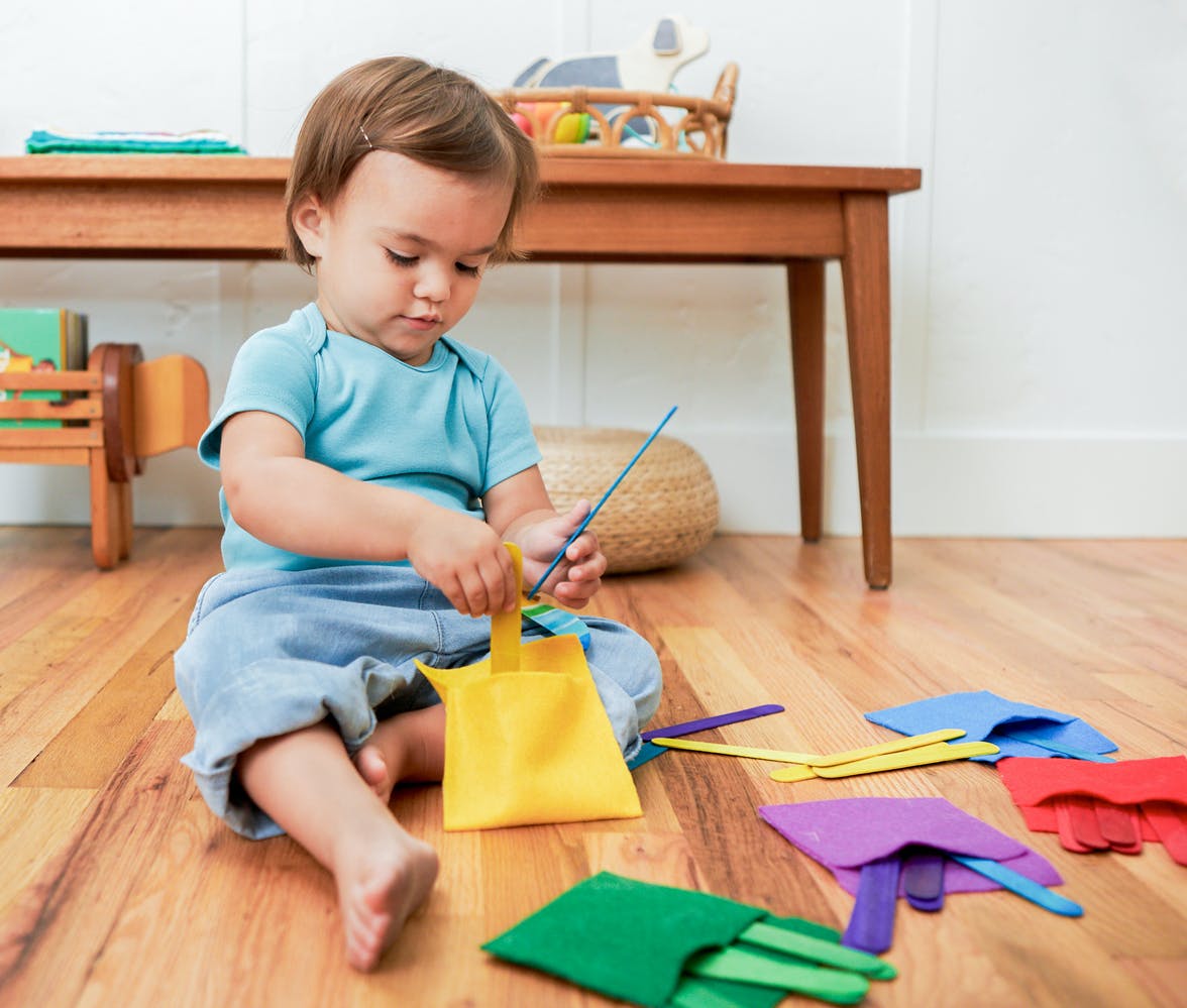 Toddler putting colored popsicle sticks into colored felt pockets