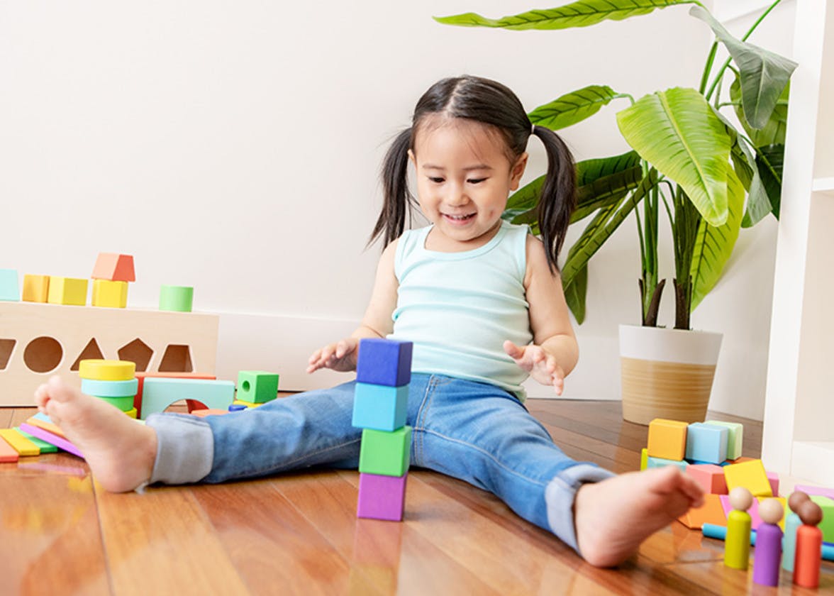 Toddler sitting on the ground stacking four blocks