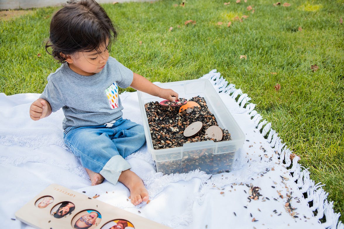 Toddler sitting outside with a container of seeds with puzzle pieces hidden in them