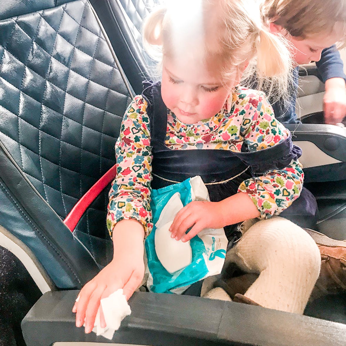 Toddler wiping down an air plane seat with wet wipes