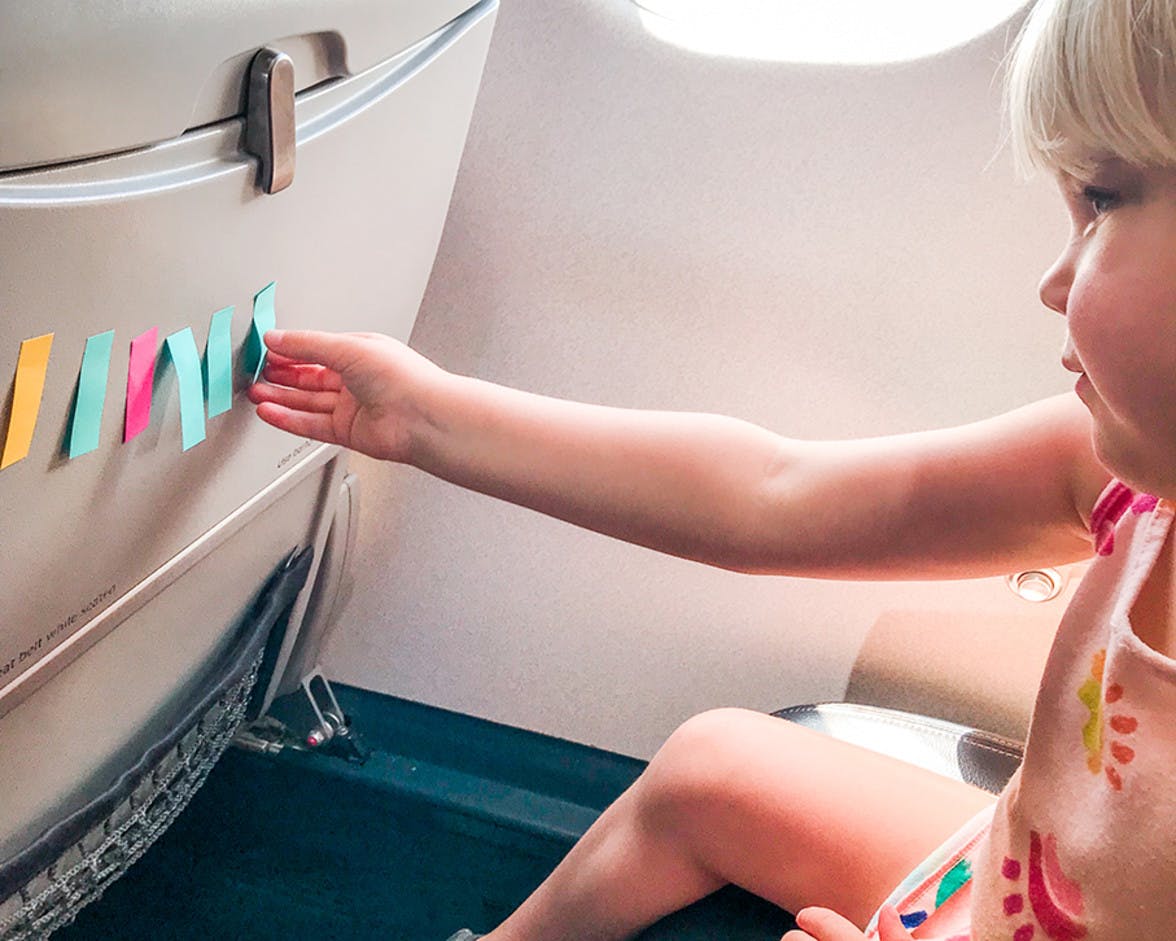 Child sitting in an air plane seat playing with post it notes