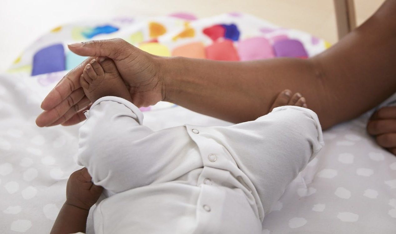 Baby kicking their feet against a woman's arm and hand