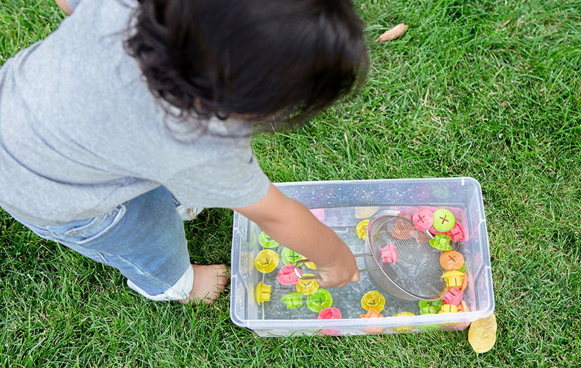 Toddler scooping out buttons from water on the grass