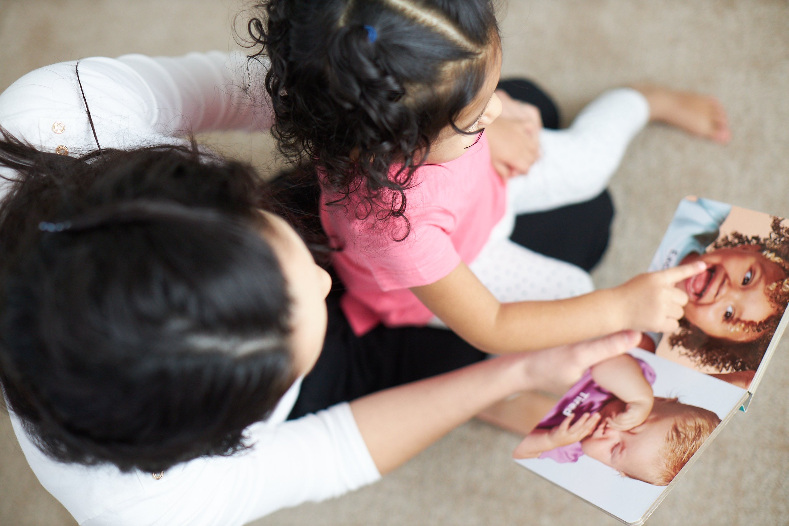 Woman holding a toddler in her lap while looking at a book by Lovevery