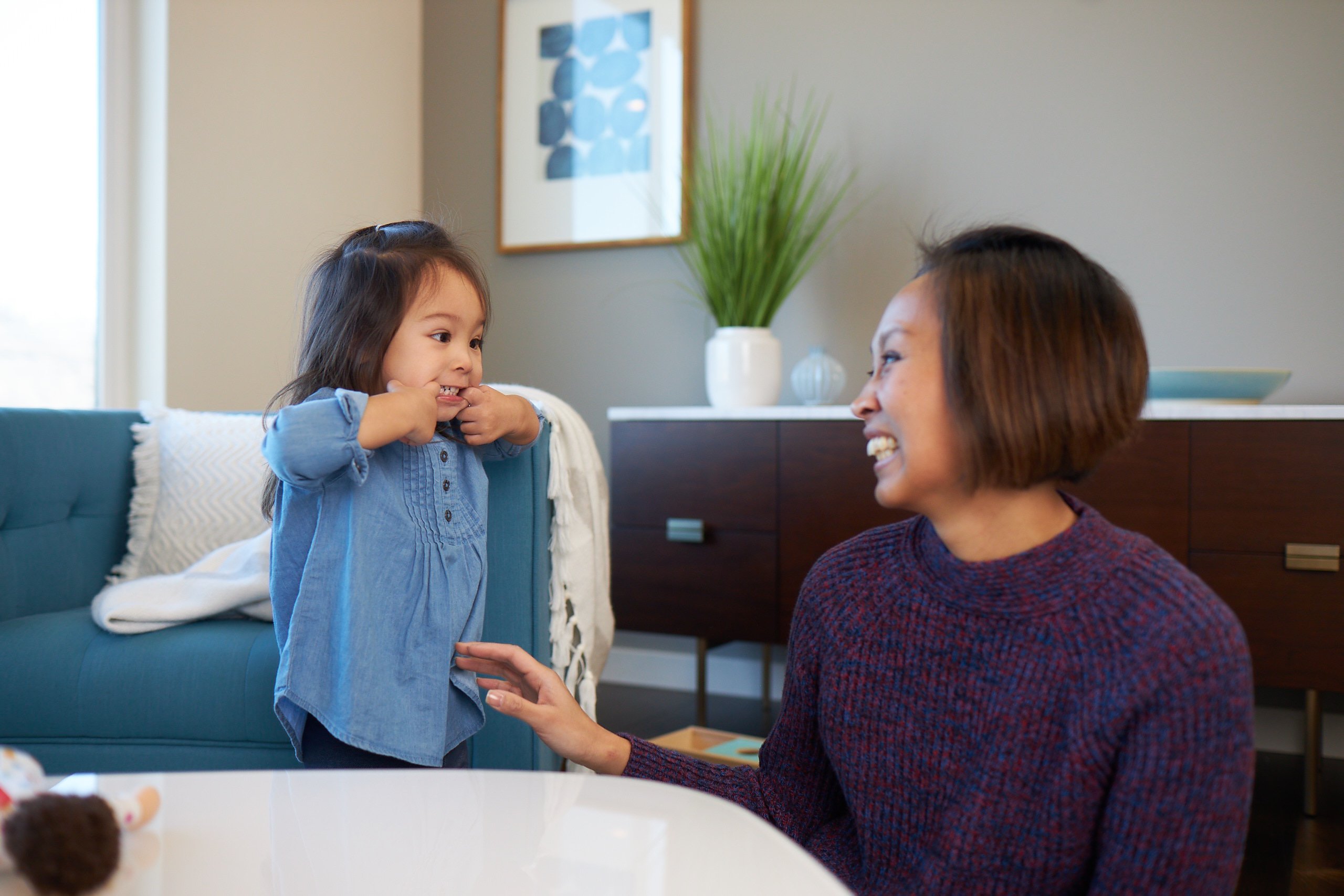 Toddler with their fingers in their mouth while a woman is laughing
