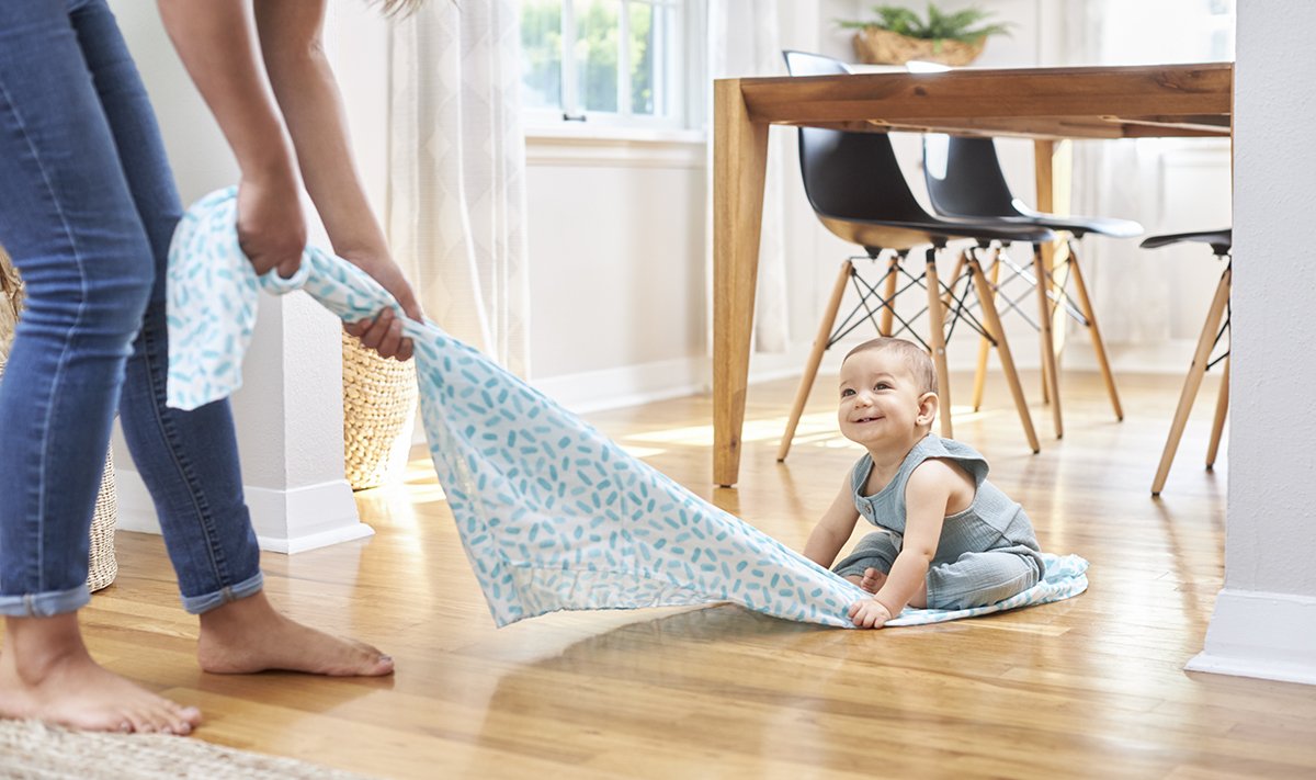 Baby sitting on a swaddle being pulled on a wood floor