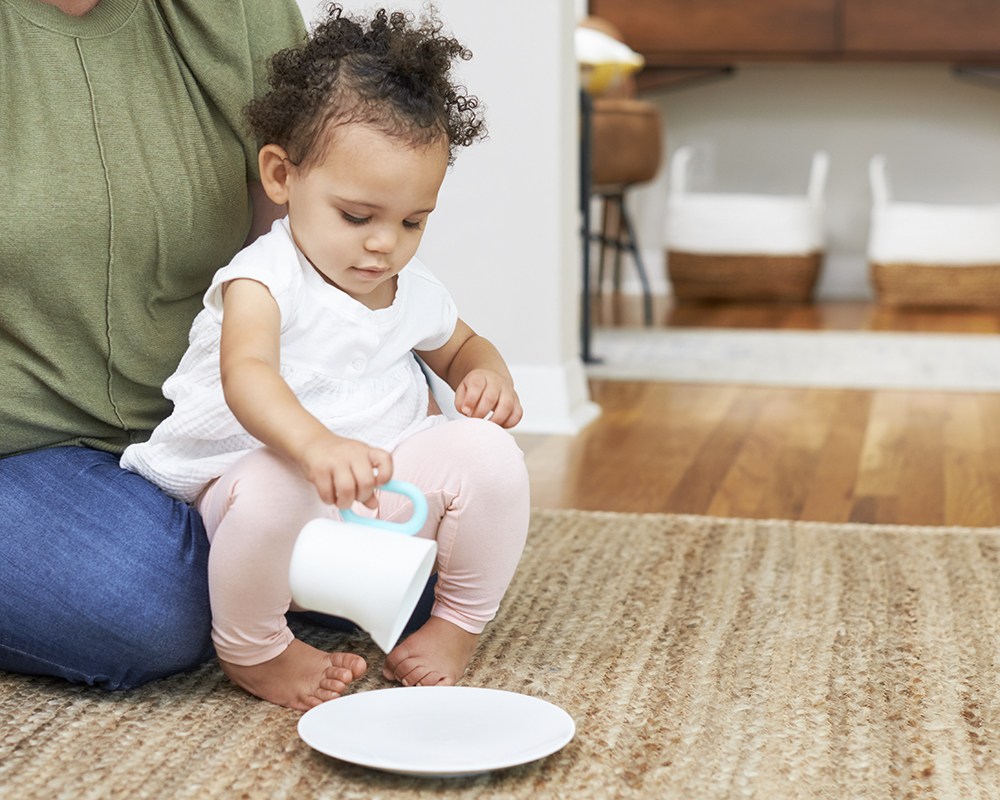 Toddler pretending to pour a liquid from a cup to a plate