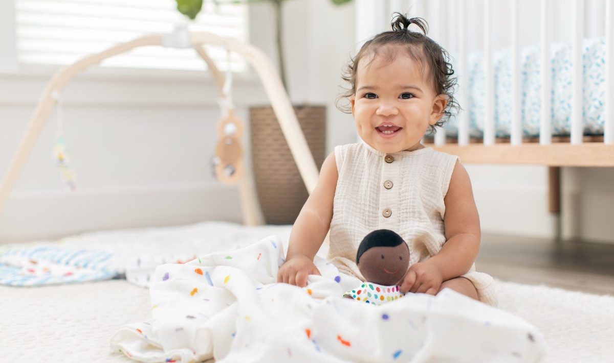 Baby sitting on the floor holding their Cotton Doll by Lovevery
