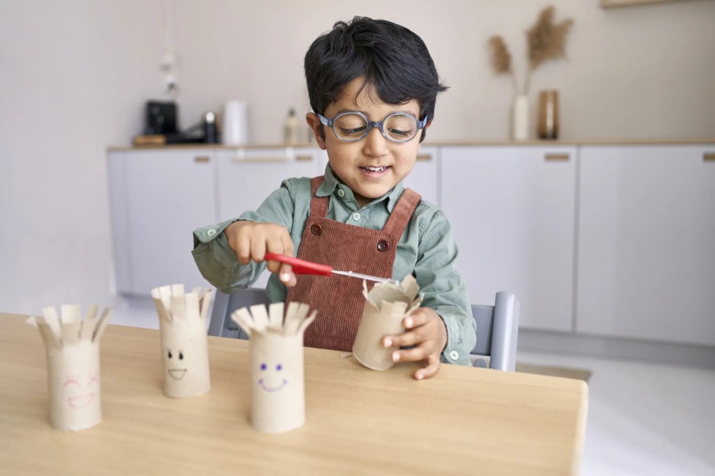 Child cutting toilet paper rolls while doing a craft